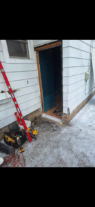 A handyman replacing an exterior door, with tools on the ground, for Helping Handyman Fox Valley LLC in Oshkosh, WI.
