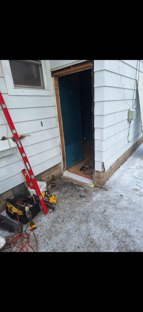 A handyman replacing an exterior door, with tools on the ground, for Helping Handyman Fox Valley LLC in Oshkosh, WI.
