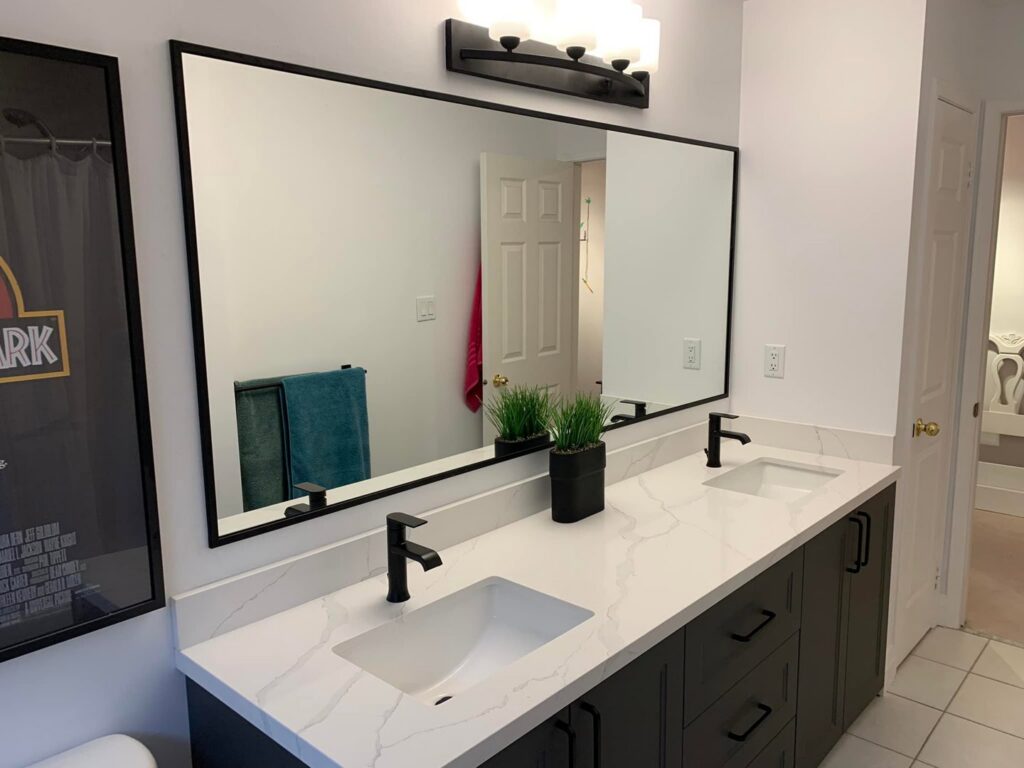 A double bathroom vanity with dark cabinets, white countertop, and black faucets by NP General Contracting in Austin, TX.