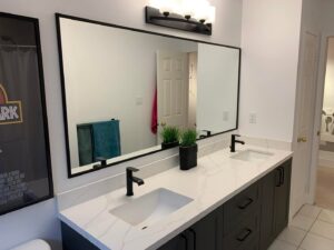 A double bathroom vanity with dark cabinets, white countertop, and black faucets by NP General Contracting in Austin, TX.