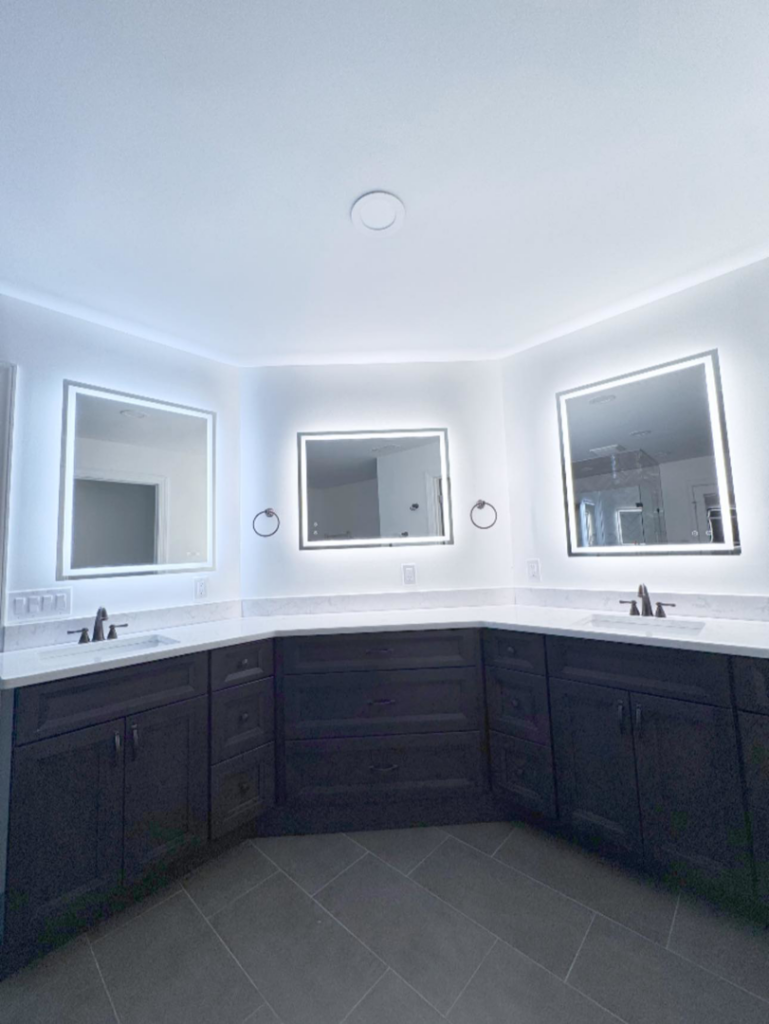 A modern bathroom featuring a double vanity with dark cabinets and illuminated mirrors installed by Shipe Builders in Salisbury, MD.