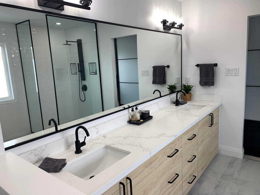 A double bathroom vanity with light wood cabinets and black faucets installed by NP General Contracting in Austin, TX.