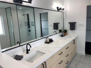 A double bathroom vanity with light wood cabinets and black faucets installed by NP General Contracting in Austin, TX.