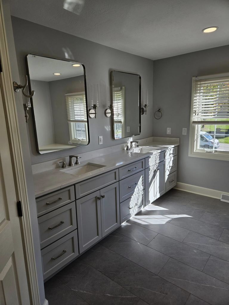 A newly renovated bathroom with a double vanity, gray cabinets, and dark tile flooring by Antalek Construction LLC in Erie, PA