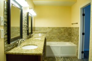 A newly remodeled bathroom featuring a double vanity with granite countertops, a tiled backsplash, and a clean bathtub by Custer Remodeling in Plano, TX.