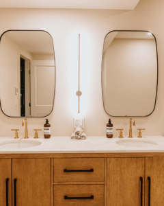 A stylish double vanity with gold faucets and modern mirrors, part of a bathroom remodel by Knaub Home Solutions in Rochester, NY.