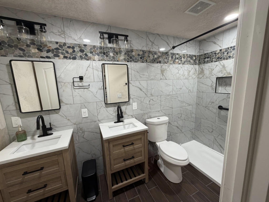 A renovated bathroom with double vanities, new fixtures, and a tiled shower by RK Pro Service Inc in Colorado Springs, CO.