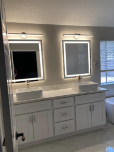 A beautifully remodeled bathroom with a double vanity, vessel sinks, and illuminated mirrors by J.C.Improvement in Katy, TX.