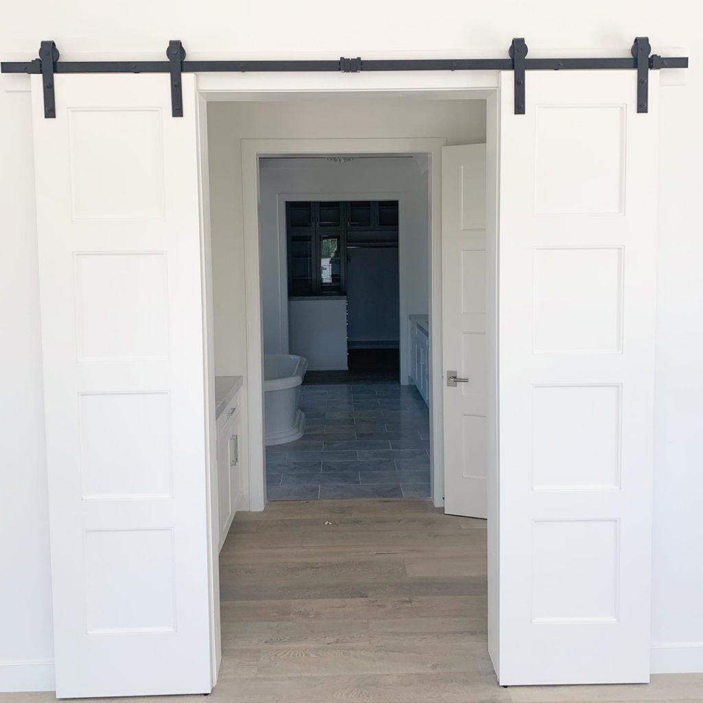 Double white barn door installation leading to a bathroom by Mountain Door and Trim in Phoenix, AZ.