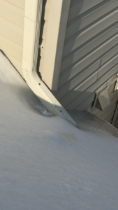 A house downspout partially covered by snow on a roof, showing a potential need for gutter and downspout maintenance by Crown Remodeling in Owings Mills, MD.