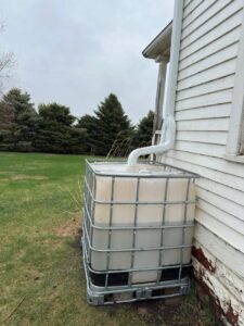 A downspout directing rainwater into a large collection tank, installed by The Brothers that just do Gutters in Sioux Falls, SD.