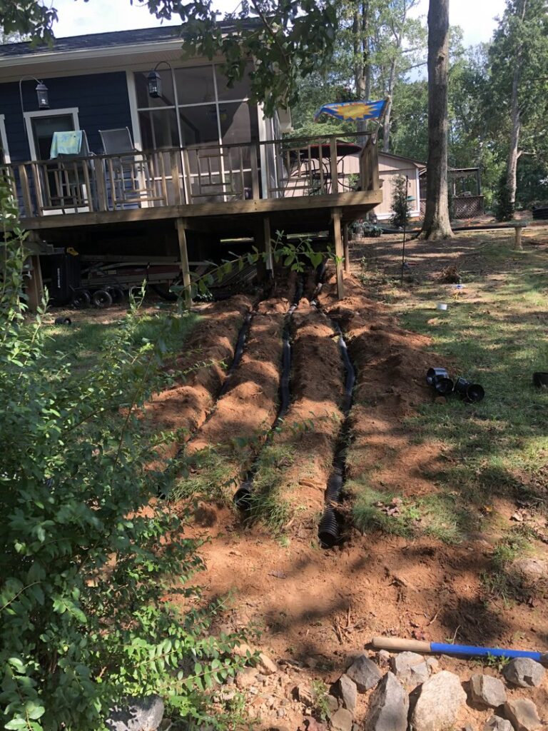 Drainage pipes being installed in trenches in a backyard by Drip Dry Drainage in Cramerton, NC.
