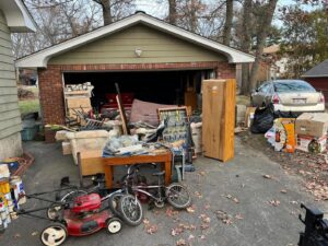 A residential driveway and garage overflowing with various junk items, ready for removal by Tj's junk removal LLC in Derry, NH.