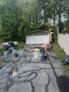 A handyman sealing cracks in an asphalt driveway for Power Pro Painting in Cleveland, OH