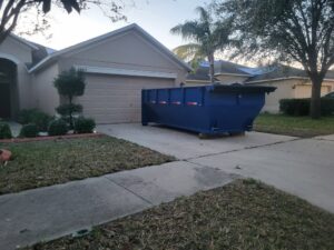 An empty blue dumpster placed on a residential driveway for junk removal by R&Y Dumpster Kings in Tampa, FL.