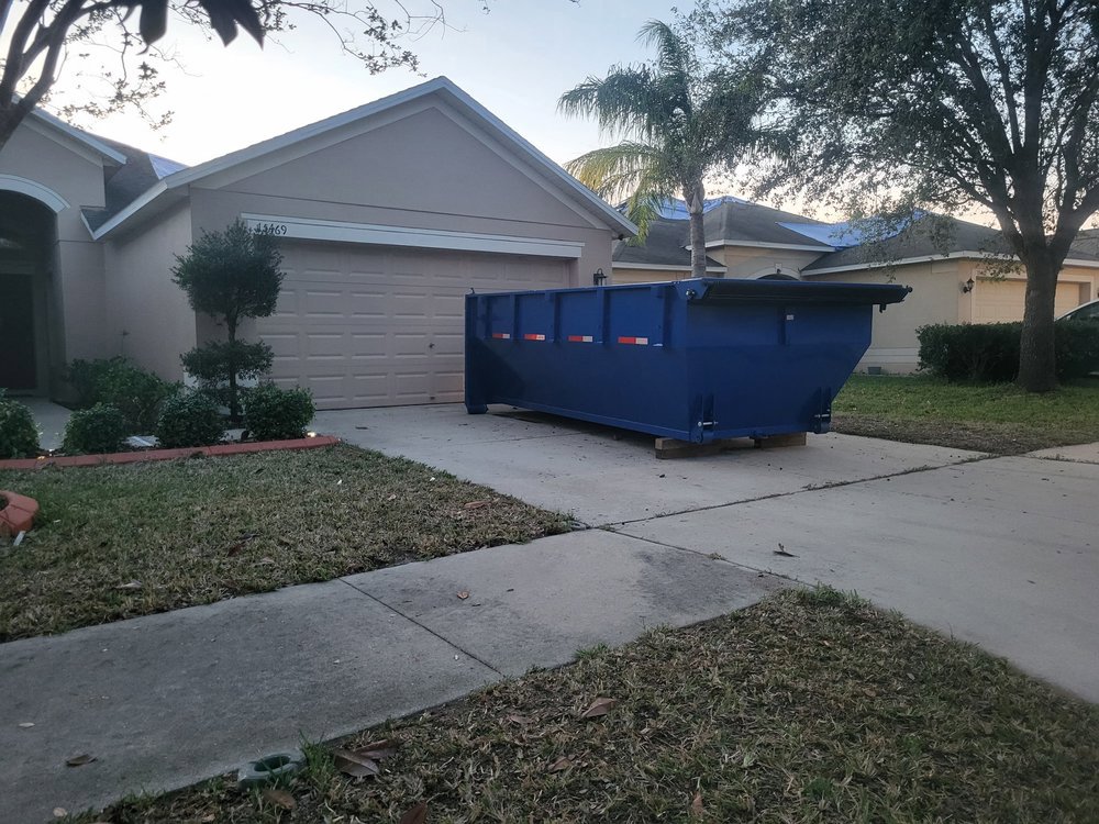 An empty blue dumpster placed on a residential driveway for junk removal by R&Y Dumpster Kings in Tampa, FL.