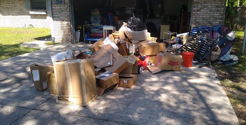 A residential driveway piled high with cardboard boxes, old furniture, and various household junk for removal by Jax Junk Squad in Jacksonville, FL.