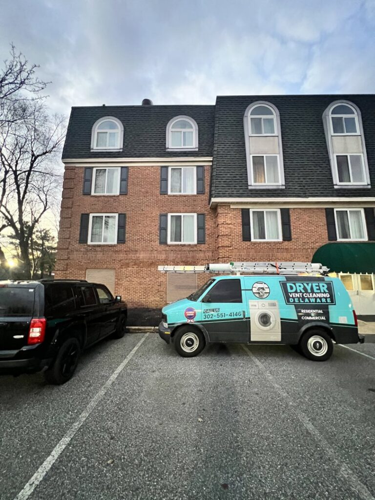 The Dryer Vent Cleaning of Delaware service van parked in front of a multi-story apartment building in Wilmington, DE.