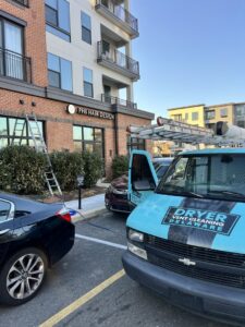 The Dryer Vent Cleaning of Delaware service van and a ladder at a commercial job site in Wilmington, DE.