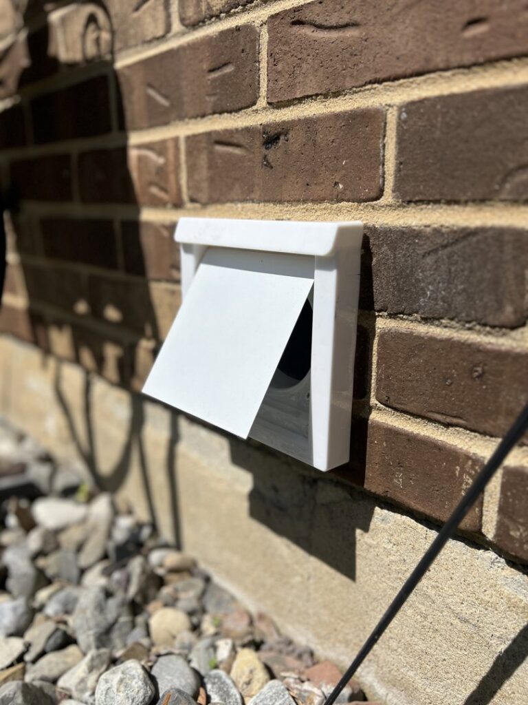A white dryer vent cover on a brick exterior wall, ready for or after cleaning by Dryer Vent Cleaning of Delaware in Wilmington, DE.
