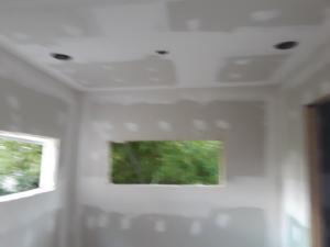 Drywall installed on the ceiling and walls of a room, showing recessed lighting holes, by D&B Drywall in Canton, OH.