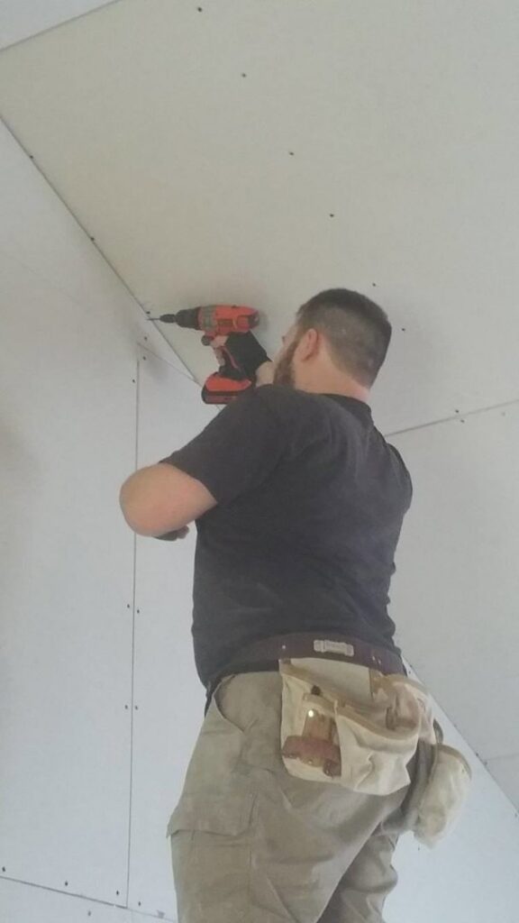 A handyman installing drywall on a ceiling using a drill, a service provided by GCB Home Improvement in Appleton, WI.