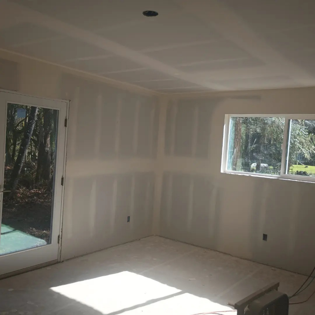 A finished drywall corner of a room with a window and door, completed by JLSL Drywall LLC in Salem, OR.
