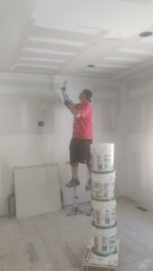 A skilled drywall finisher on stilts applying mud to a ceiling, showcasing expert work by NED CO. in Springfield, MA.