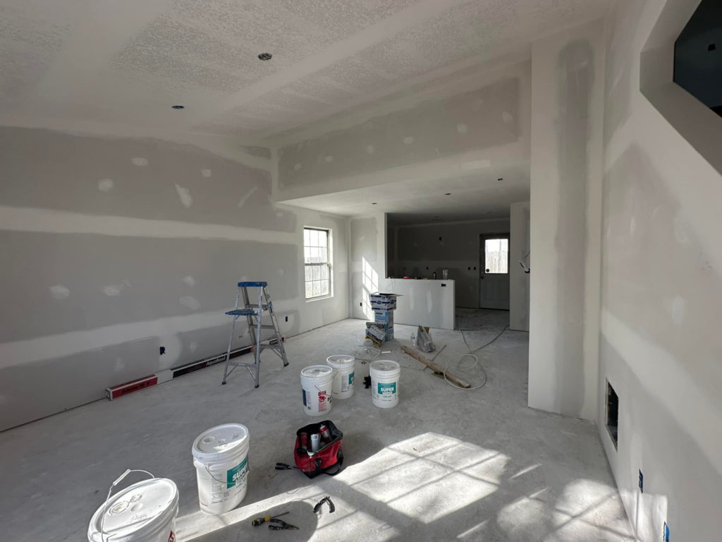 An interior room with new drywall taped and mudded, along with painting supplies, indicating renovation work by One Seven Painting LLC in Columbia, MO.