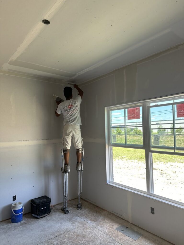A worker on stilts applying drywall mud to a ceiling, performing drywall finishing for Hahn Brothers Drywall Co Inc in Evansville, IN