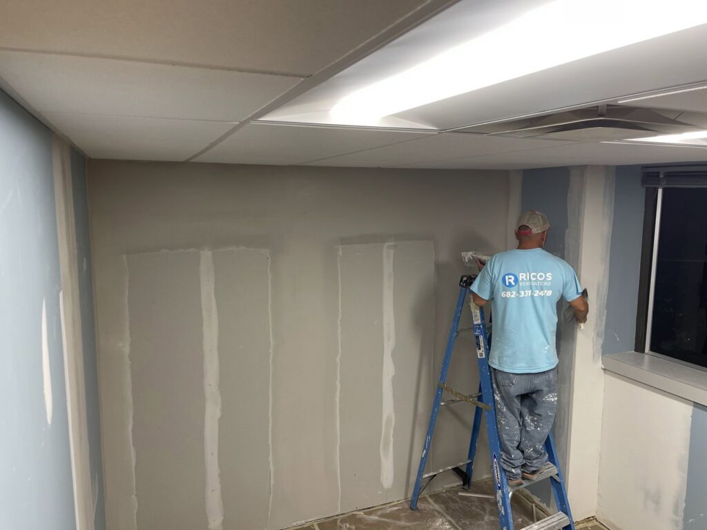 A worker from Ricos Renovations applying drywall finishing on a ladder in Arlington, TX