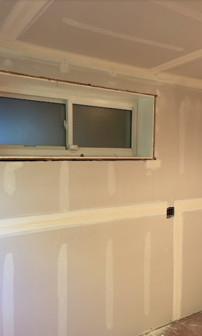 A room with new drywall installation, showing taped seams and a window, indicating construction work by Ruach Home Services in Laurel, MD.