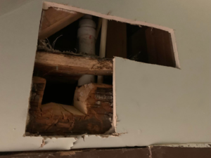 A large opening in a wall or ceiling revealing plumbing pipes and wooden structural elements, indicating a repair job by PG Painting and Contracting Services in Cincinnati, OH.
