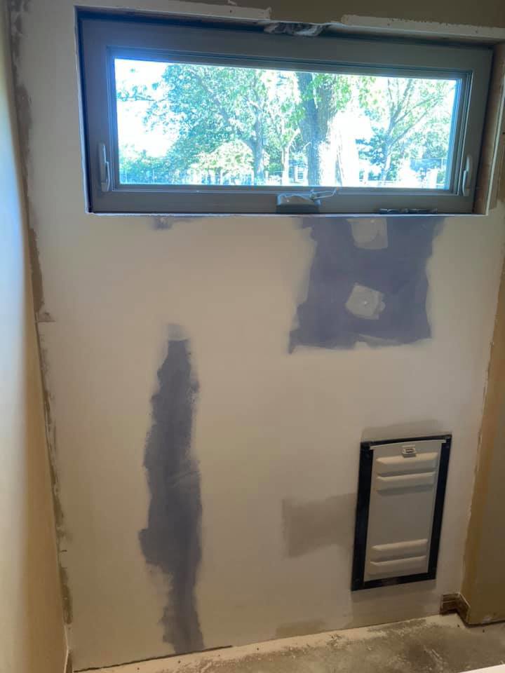An interior wall with fresh drywall patching and an access panel installed below a window, completed by AON Construction and Remodeling LLC in Wichita, KS.