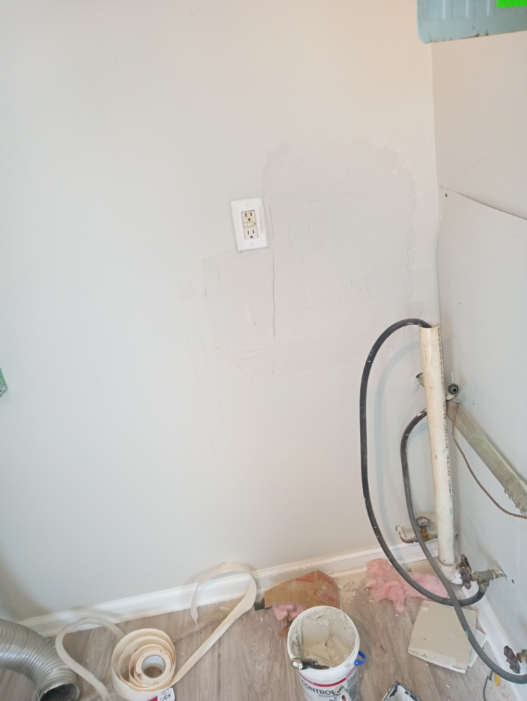 A wall with patched areas and an electrical outlet, indicating drywall repair by Charles and Drew Project Page in Detroit, MI.