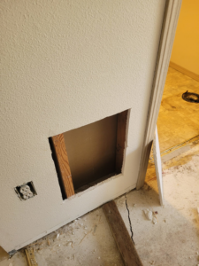 A wall with a large drywall cutout revealing studs, indicating repair work by Precision Craftsman LLC in San Antonio, TX.