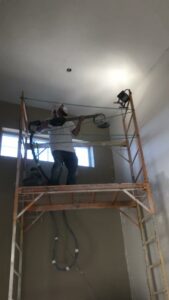 A worker on scaffolding performing drywall sanding during an interior renovation by Finesse Painting and Remodeling in Fort Worth, TX.
