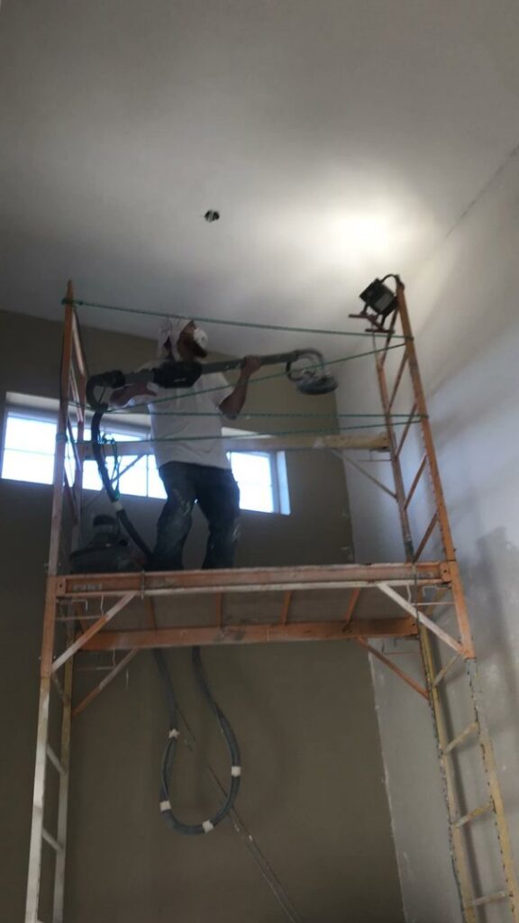 A worker on scaffolding performing drywall sanding during an interior renovation by Finesse Painting and Remodeling in Fort Worth, TX.