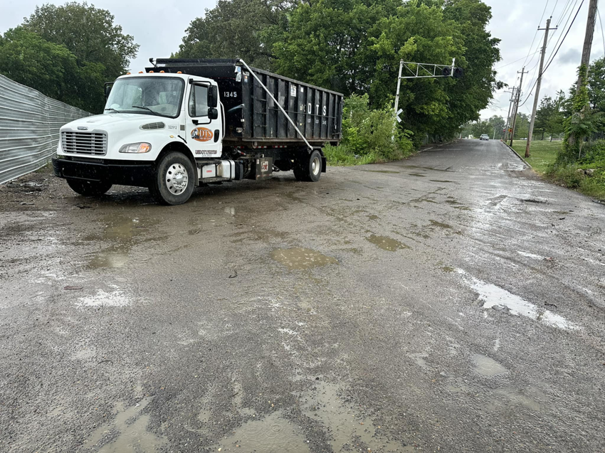 A Dts dumpster rentals truck with an empty dumpster parked on a wet, unpaved road in Memphis, TN.
