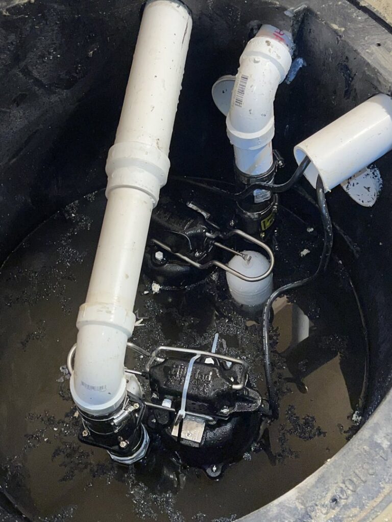 A dual sump pump system with pipes and float switches installed in a basement pit by B-Dry System of New England in North Billerica, MA.