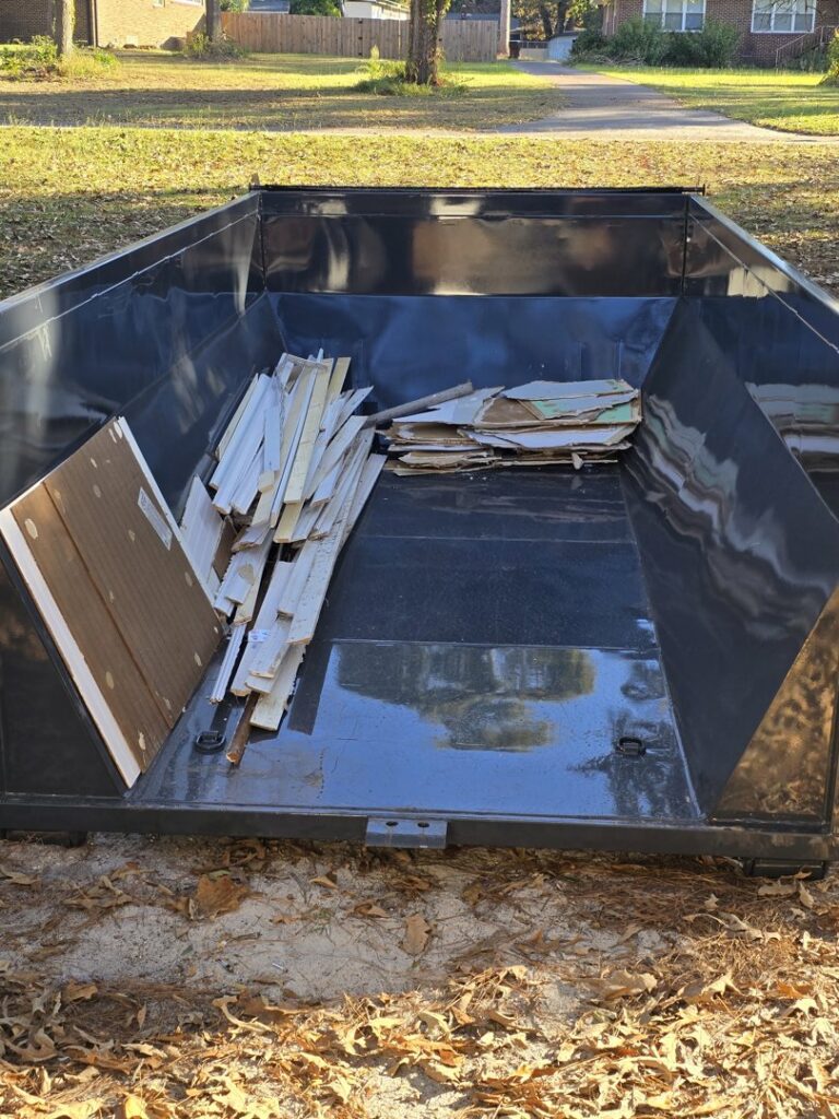 A black roll-off dump container with wood scraps and cardboard inside, ready for general junk removal by Lewis Outdoor Services LLC in Augusta, GA.