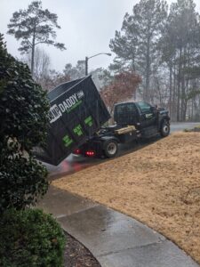 A Dump Daddy truck picking up a full junk removal dumpster from a residential property in Buford, GA.