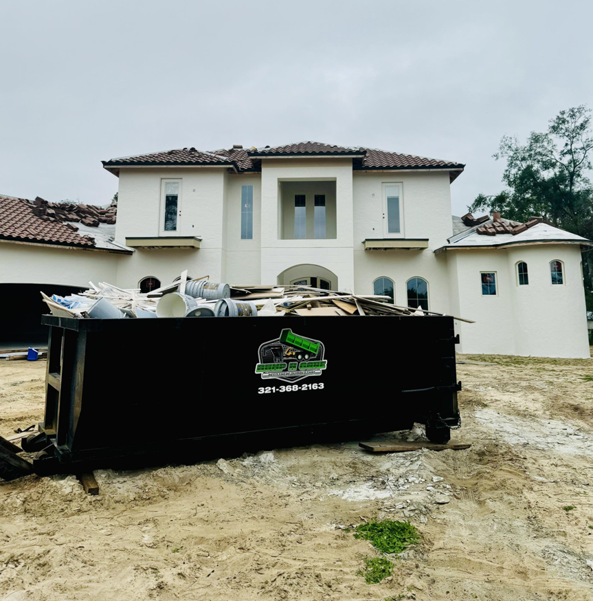 A Dump N Gone dumpster full of renovation debris in front of a large residential house under construction in Apopka, FL.