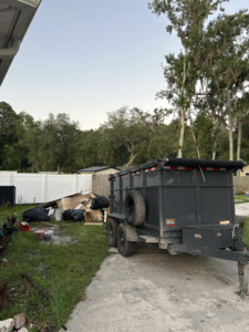 A dump trailer parked next to a large pile of debris and trash bags for removal by Just Dump It in Jacksonville, FL.