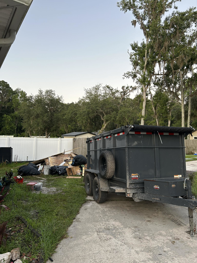 A dump trailer parked next to a large pile of debris and trash bags for removal by Just Dump It in Jacksonville, FL.