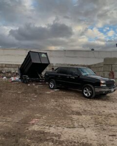 A black pickup truck with a raised dump trailer at a junk removal site, indicating a completed or in-progress job by We-Haul Junk Removal in Long Beach, CA