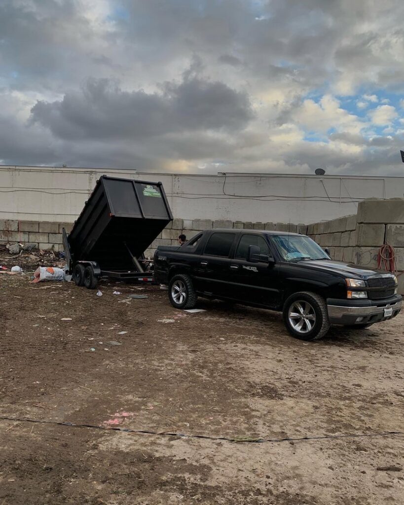 A black pickup truck with a raised dump trailer at a junk removal site, indicating a completed or in-progress job by We-Haul Junk Removal in Long Beach, CA