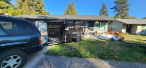 A dump trailer parked in front of a house with a pile of construction debris ready for removal by AG Junk Haulers in Salem, OR.