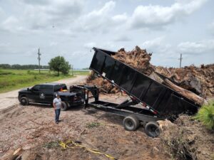 A Silverback Dumpster Rentals dump trailer actively offloading a large pile of tree roots and vegetation in LaBelle, FL.