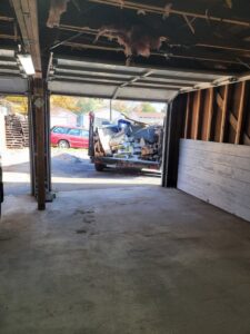 A dump trailer filled with construction debris and bags of material, seen from inside a garage, by Primetime Hauling and Junk Removal in Spokane, WA.